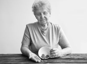 Financial industry fraud elderly woman holding bowl with a couple of coins in hand looking down sad